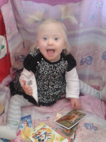 Dívka s Downovým syndromem si hraje na zemi